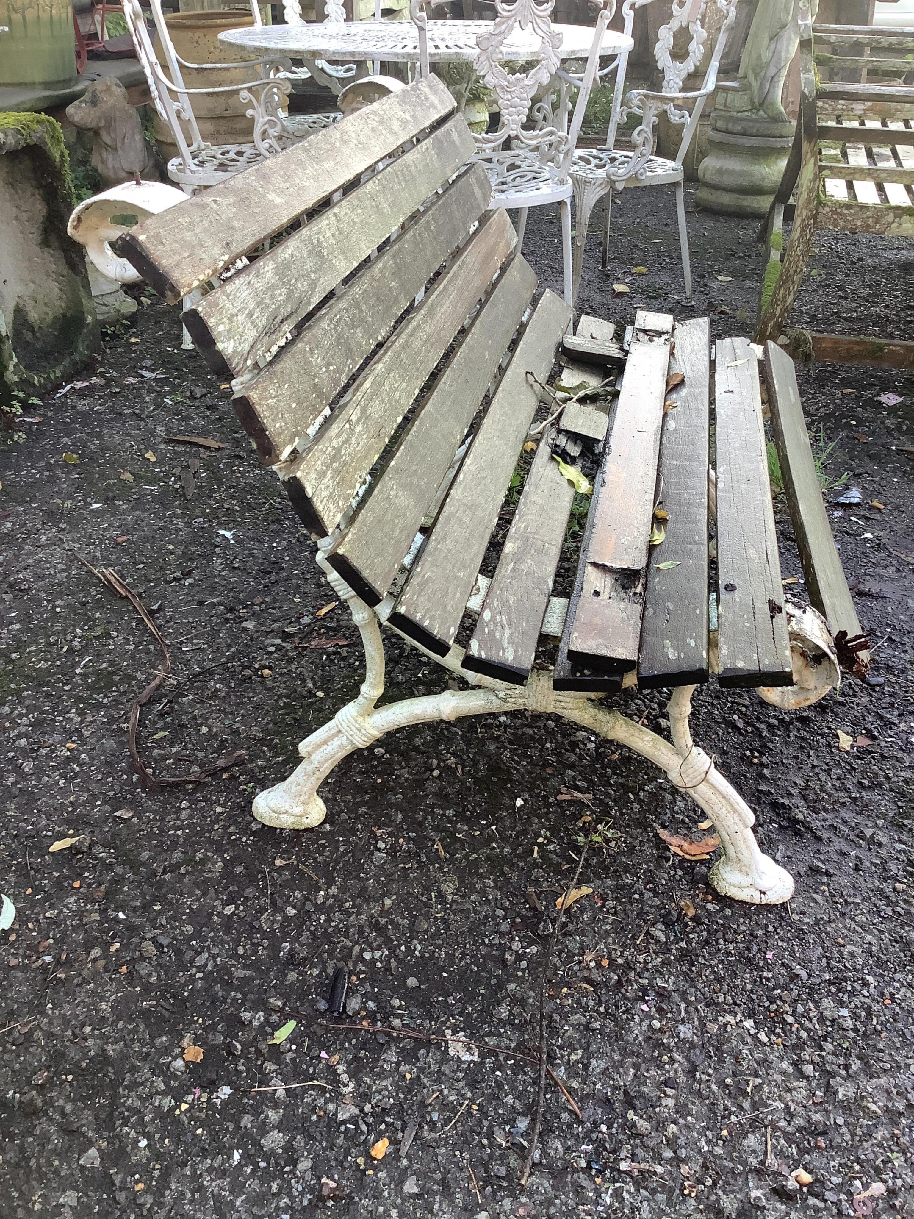 A Victorian slatted teak garden bench, raised on white painted cast iron ends, width 109cm, depth 70cm, height 74cm. Condition - poor